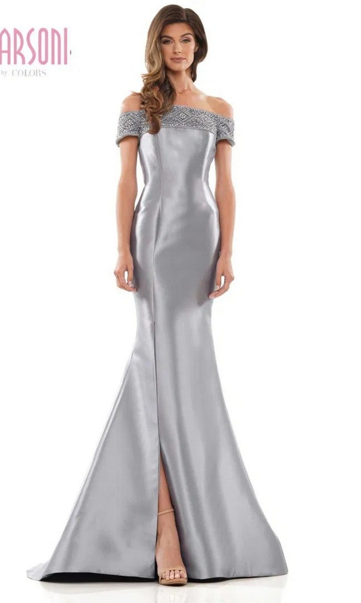 A woman stands against a white background wearing the Marsoni MV1184 long formal dress—a silver satin, off-shoulder gown with a fitted bodice, embellished neckline, elegant mermaid skirt, and a subtle front slit.